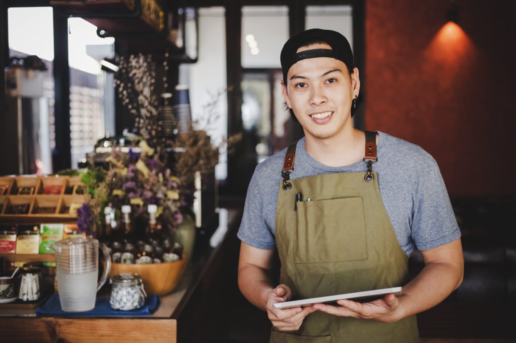 asian man barista holding tablet for checking order from customer on coffee cafe.