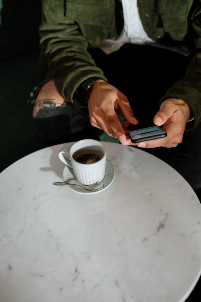 male in green coat sitting at coffee table with coffee and phone he is ordering and paying from his phone through orderup at a restaurant