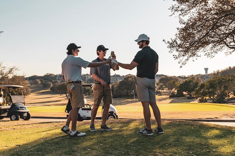 3 young men enjoying beer on a golf couruse with golf carts in the background