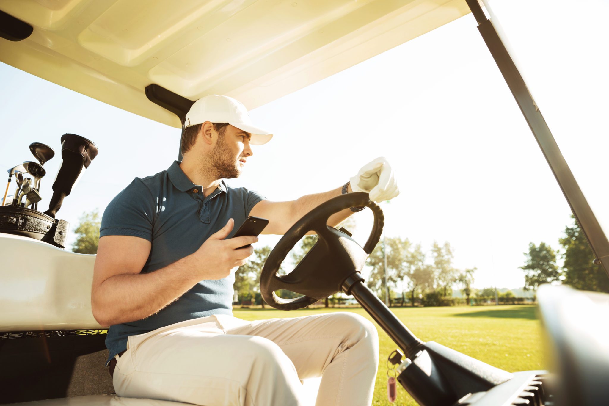 Young sportsman driving golf cart while using mobile phone
