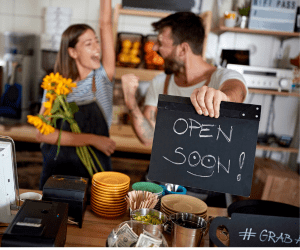 restaurant owner celebrating with his business partner holding an open soon sign showing that their new restaurant is about to open. It appears to be like a cafe with wooden accents
